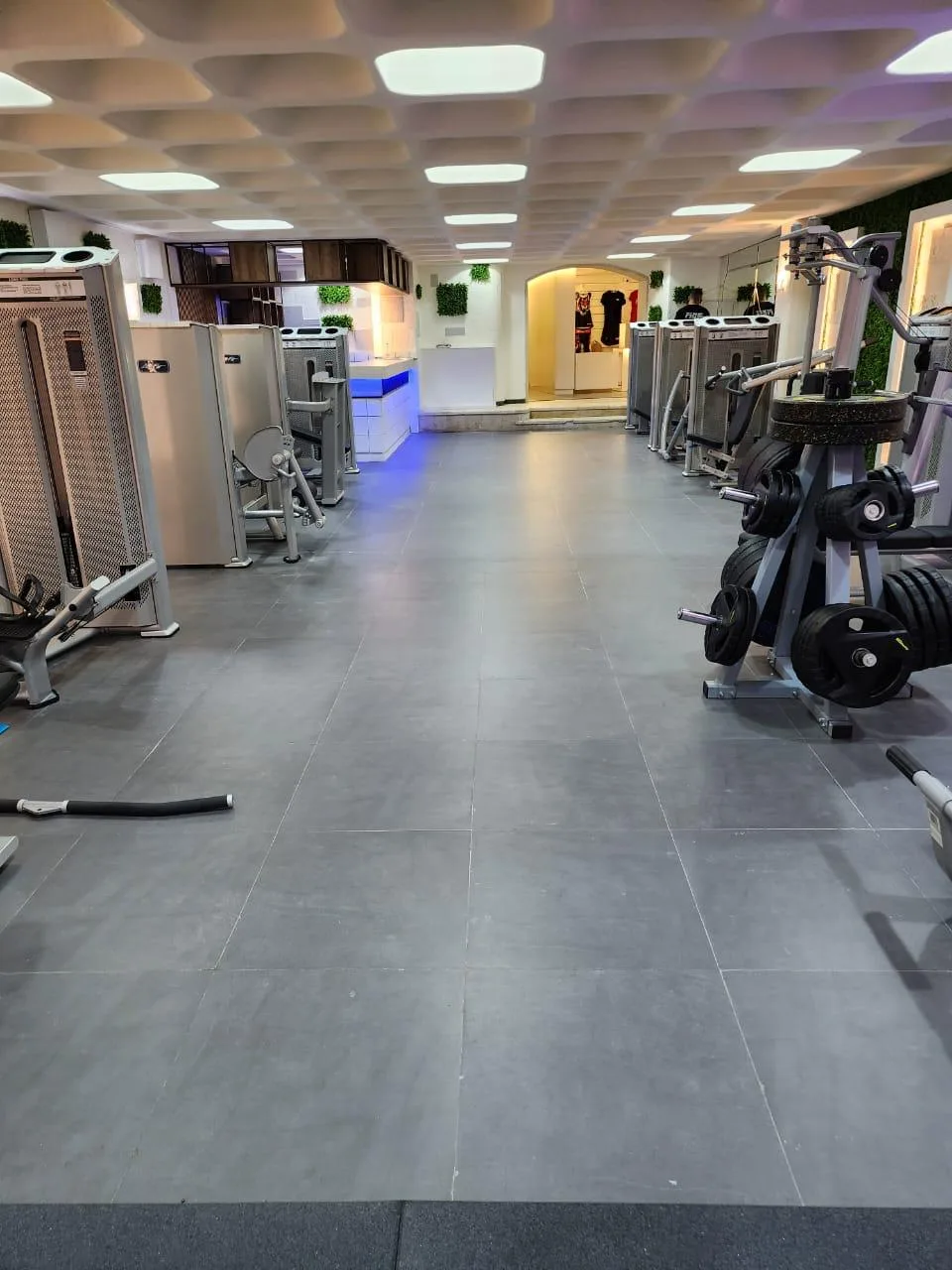 The gym floor hallway lined with machines leading to the blue lit reception counter
